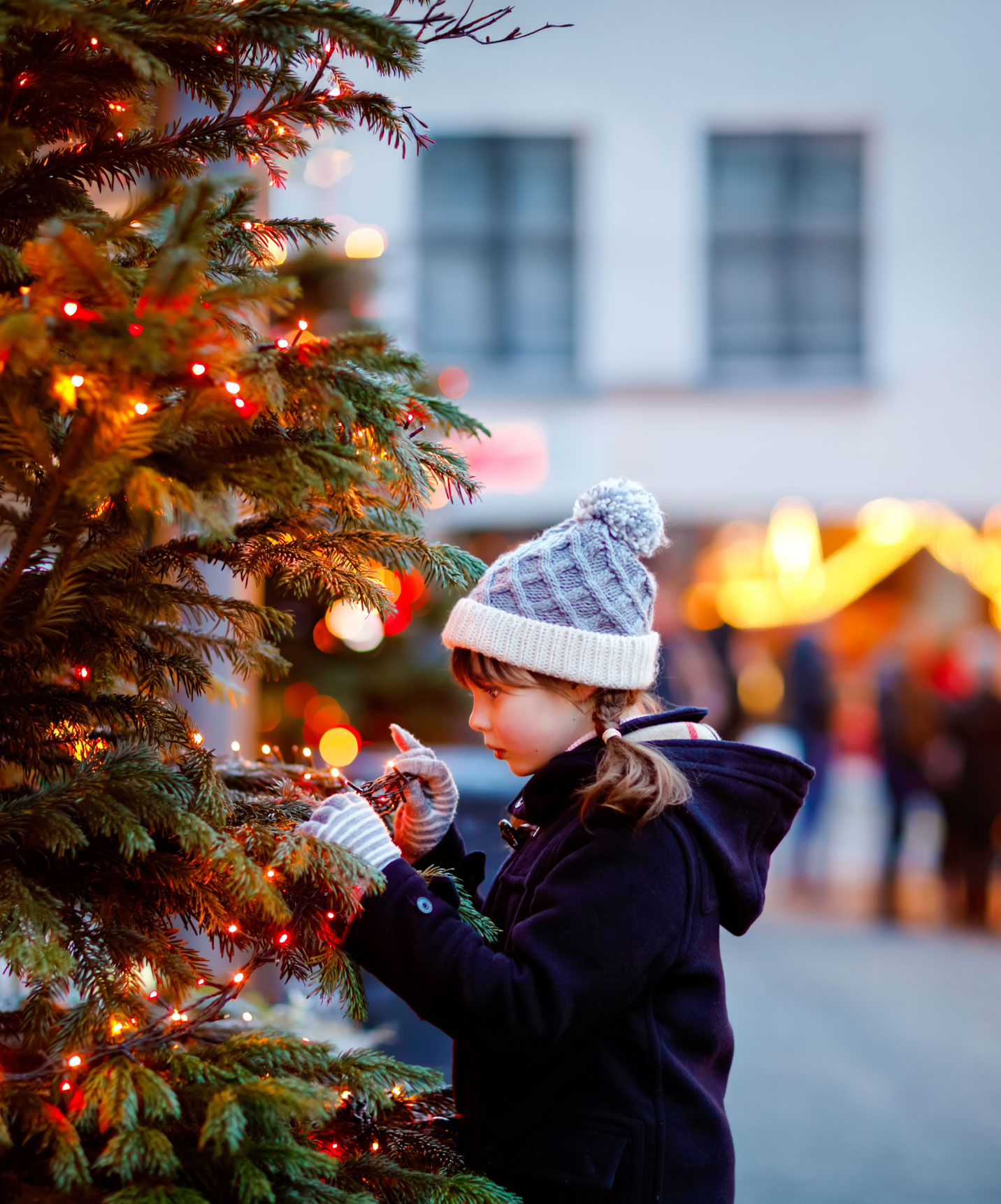 Pestana hotel com criança a decorar árvore de Natal iluminada num mercado de Natal ao entardecer festivo