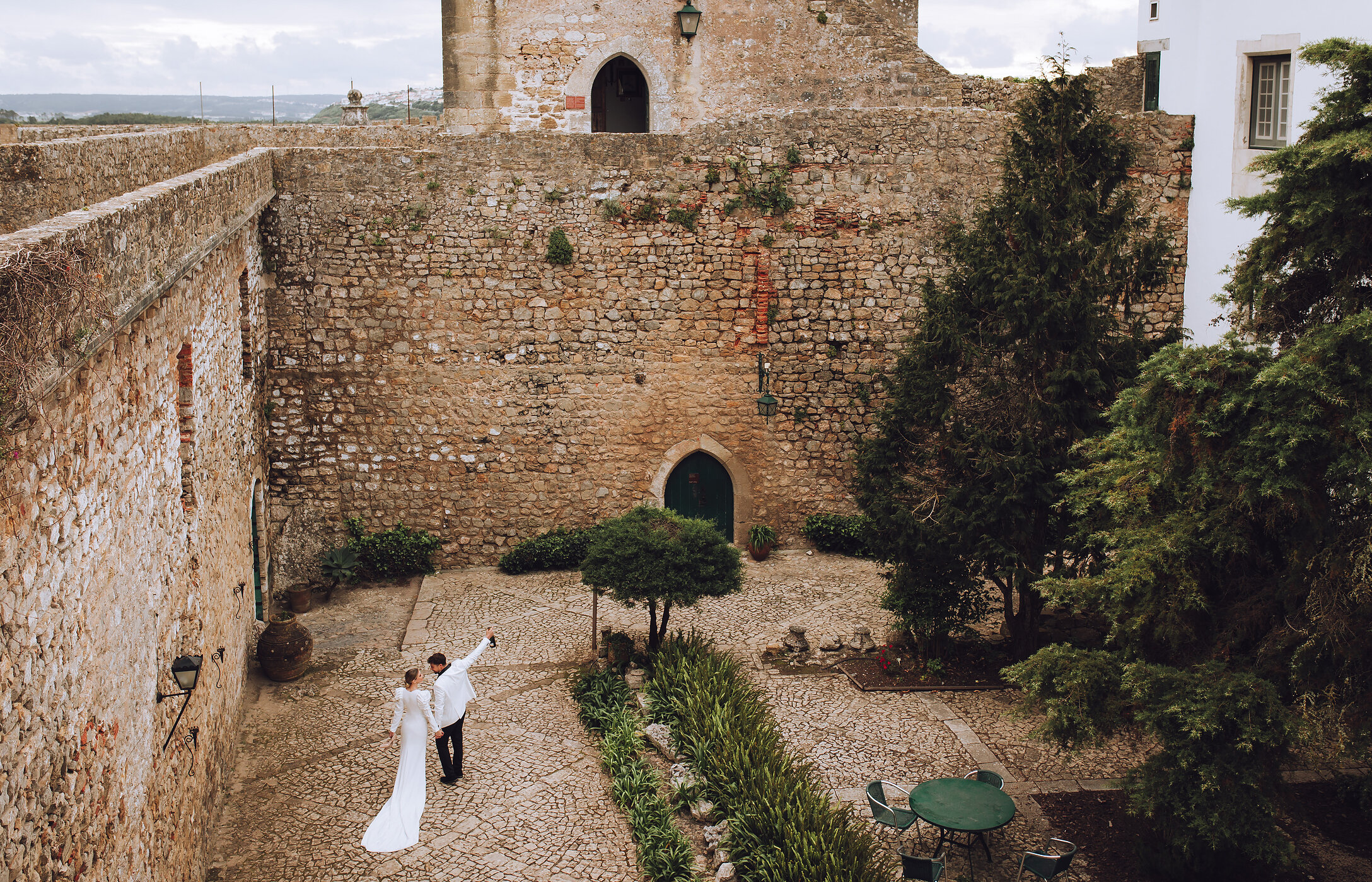 Casal recém-casado a celebrar o amor em espaço histórico, com decoração elegante e vegetação bem cuidada
