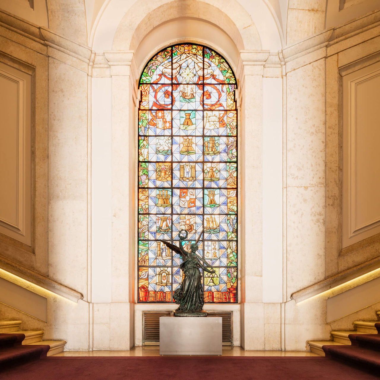 Eingangstreppe des Hotels am Terreiro do Paço mit rotem Teppich, verziertem Glasfenster und Bronzestatue