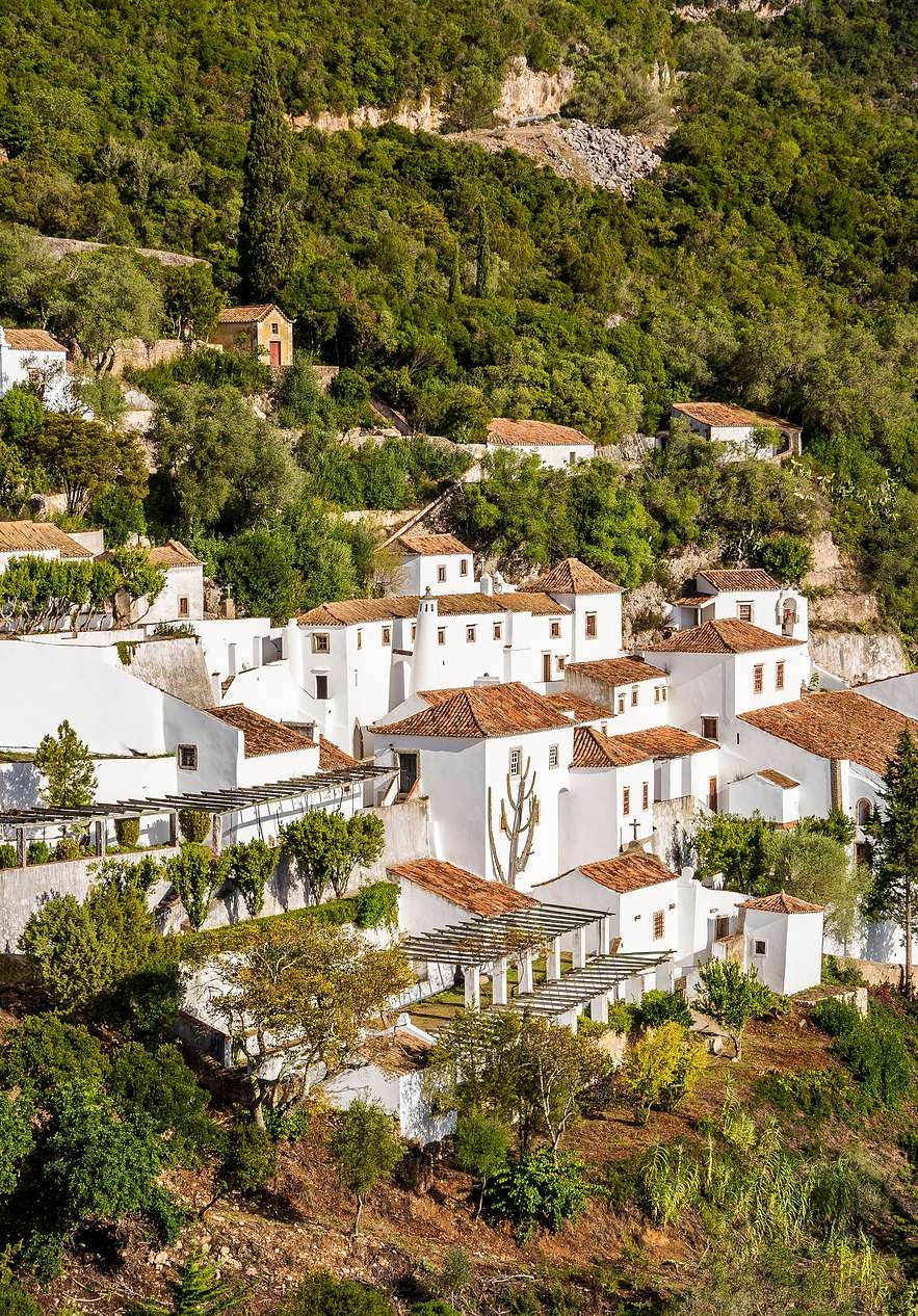 Kloster Serra da Arrábida mit mehreren weißen Gebäuden, umgeben von bergiger Landschaft und dichter Vegetation