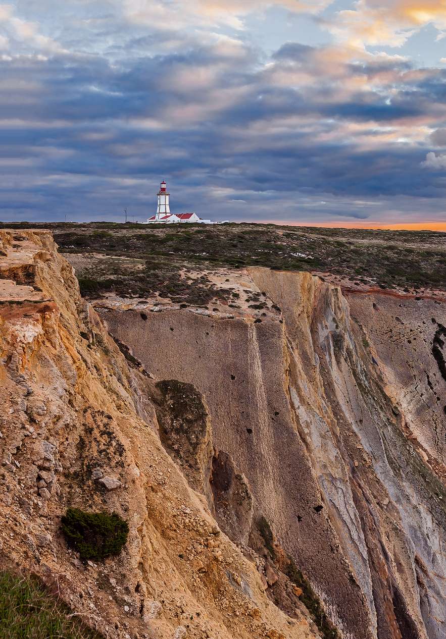 Cabo Espichel mit einem weißen Leuchtturm mit roter Kuppel neben einer Klippe und niedriger Vegetation