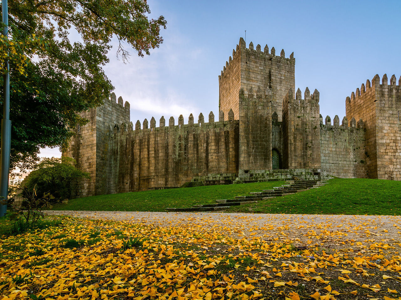 Schloss Guimarães, charakteristisch für mittelalterliche Architektur, umgeben von Gras und gefallenen gelben Blättern