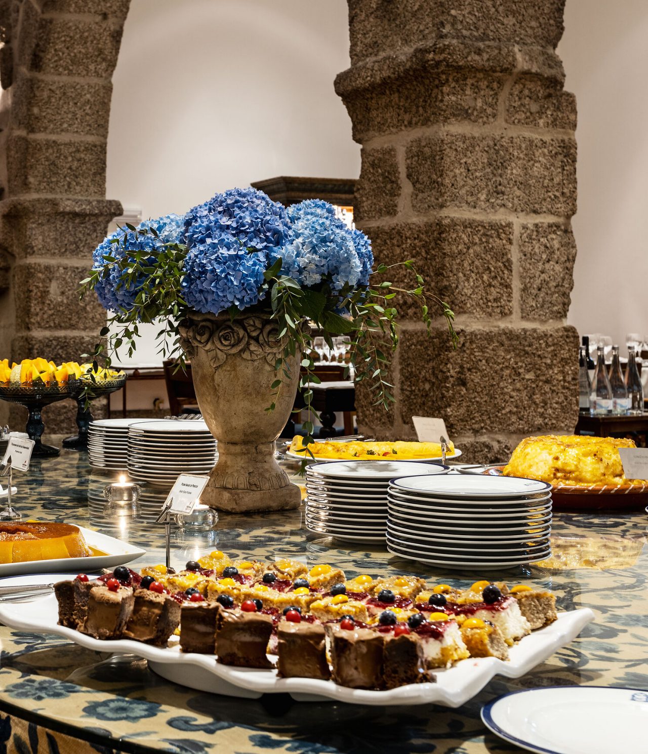 Tisch dekoriert mit einer Vielzahl von Süßigkeiten, von Kuchen und Torten bis hin zu Obst, in einem Raum mit antiken Möbeln