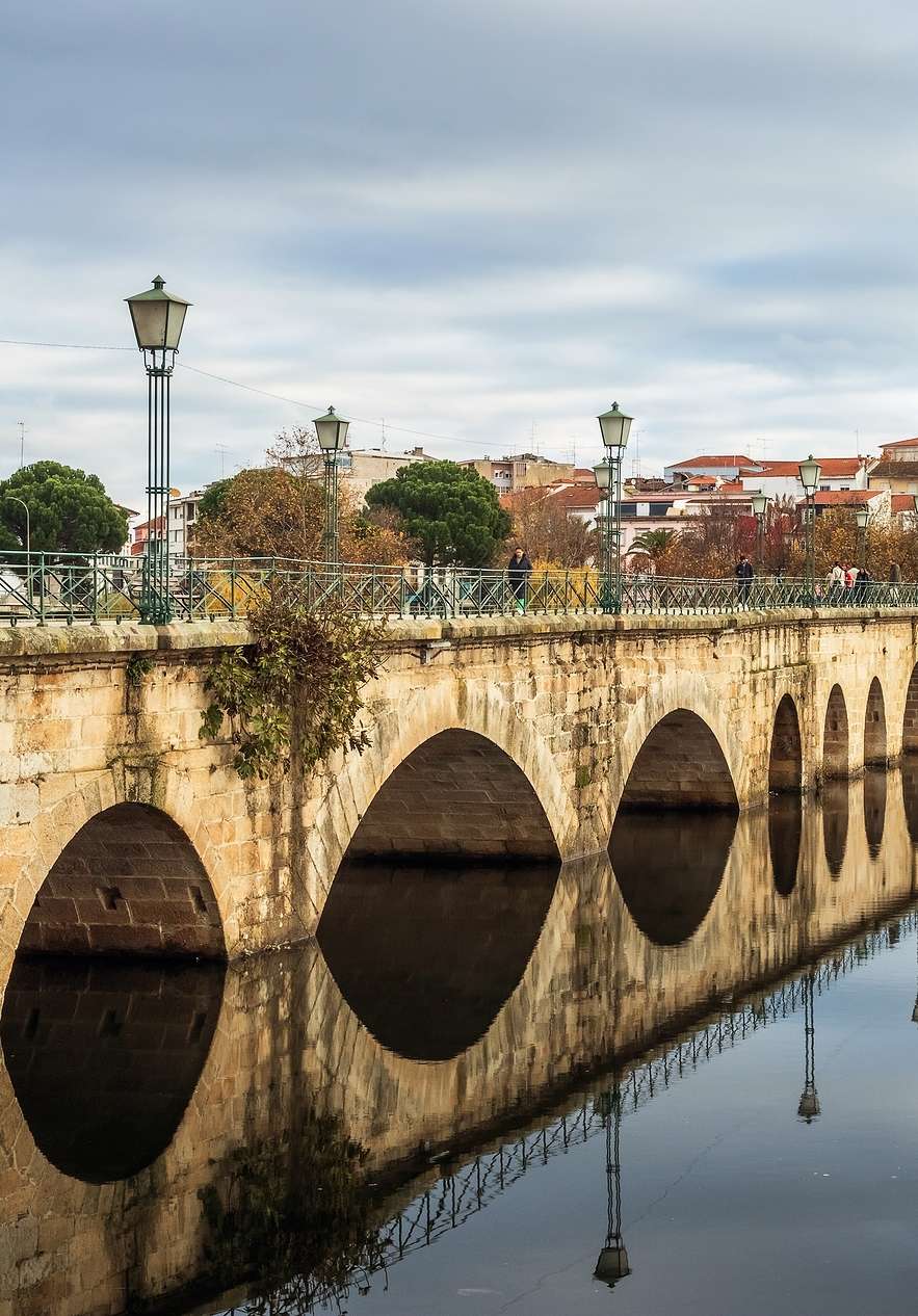 Blick auf die Ponta Medieval de Mirandela an einem ruhigen Tag mit Fluss und Wolken, mit der Stadt im Hintergrund