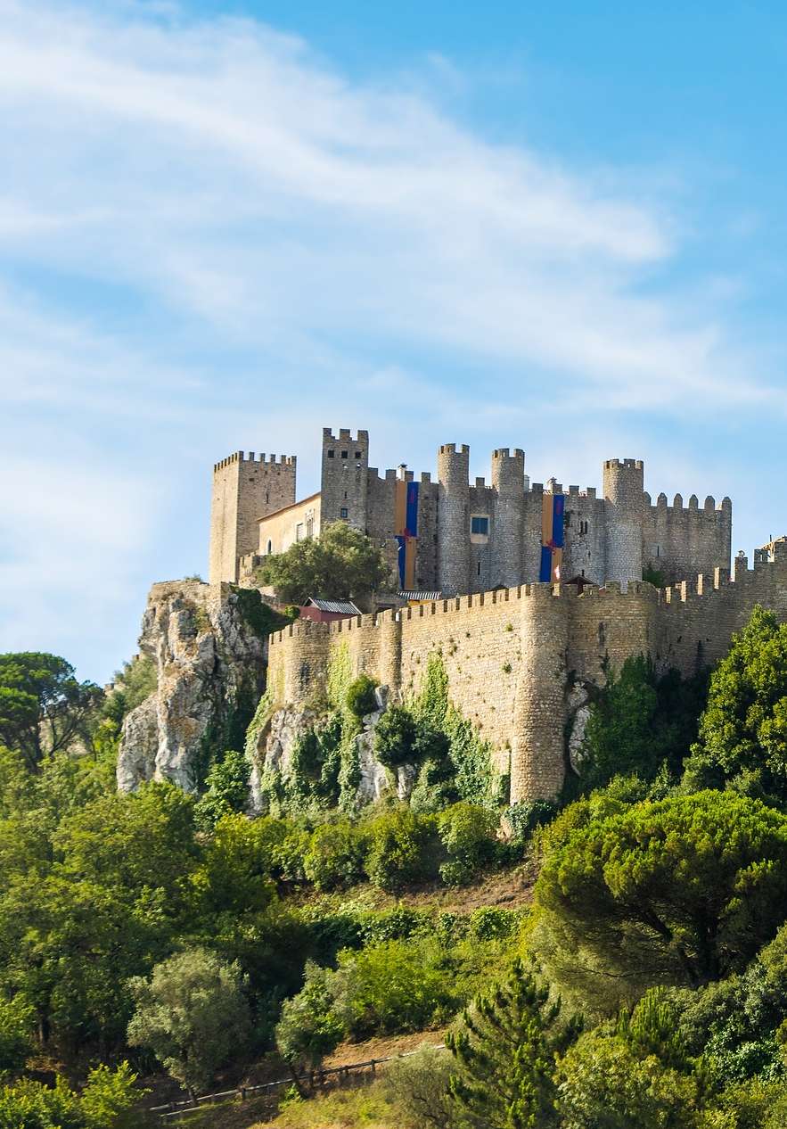 Burg Óbidos, oberhalb des mittelalterlichen Dorfes, mit Türmen und Steinmauern, die einen Kontrast zum blauen Himmel bilden