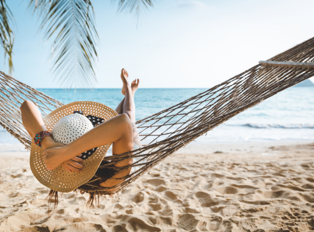 Woman relaxing in a hammock on the beach, gently swinging as she faces the calm, blue ocean