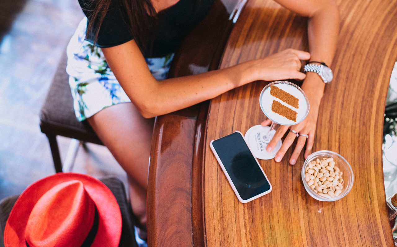 Mädchen sitzt an der Hotelbar und trinkt einen Cocktail mit einem Zimtemblem des Pestana Hotel Group