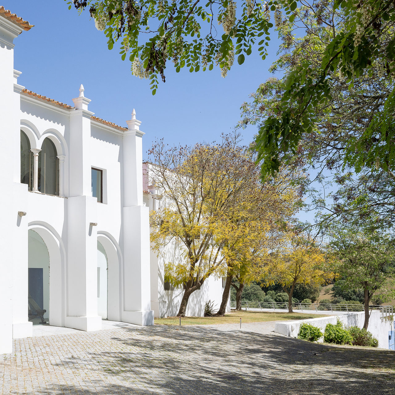 View of the facade of Pousada Convento Arraiolos, surrounded by trees and flowers of the exterior gardens