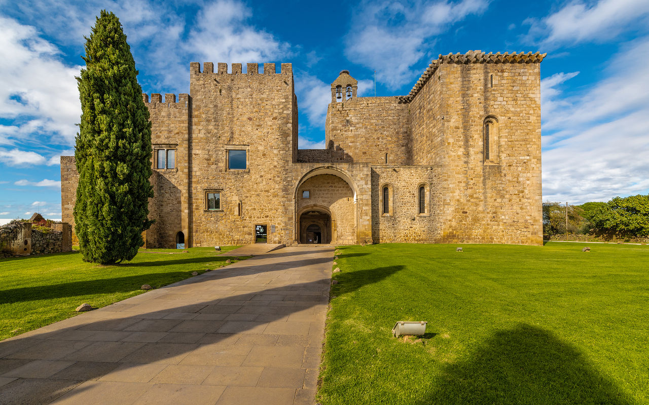 Exterior view of the stone facade of Pousada do Mosteiro do Crato, a historic hotel in Alentejo, with surrounding gardens