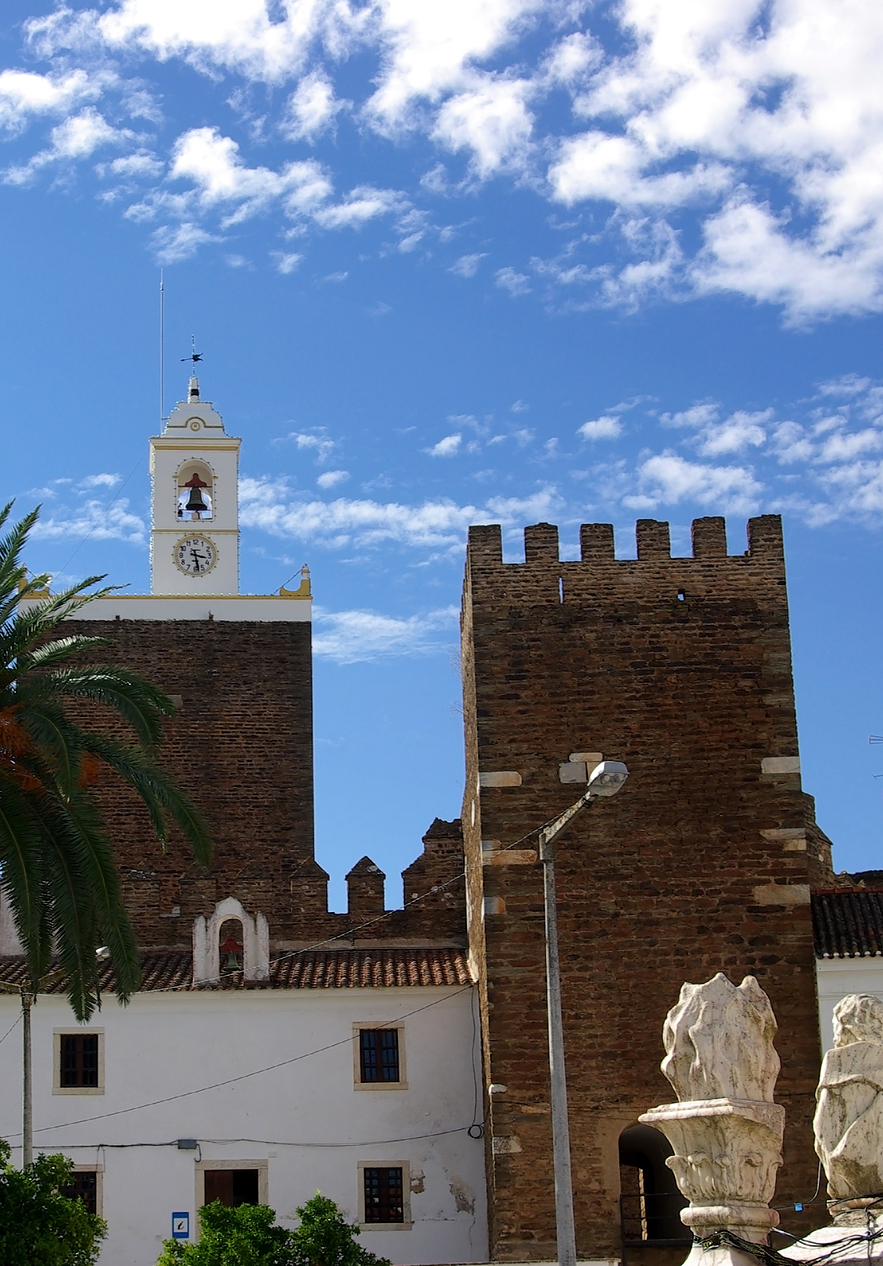 View of Alandroal castle with its stone tower and a bell on top with palm trees in front