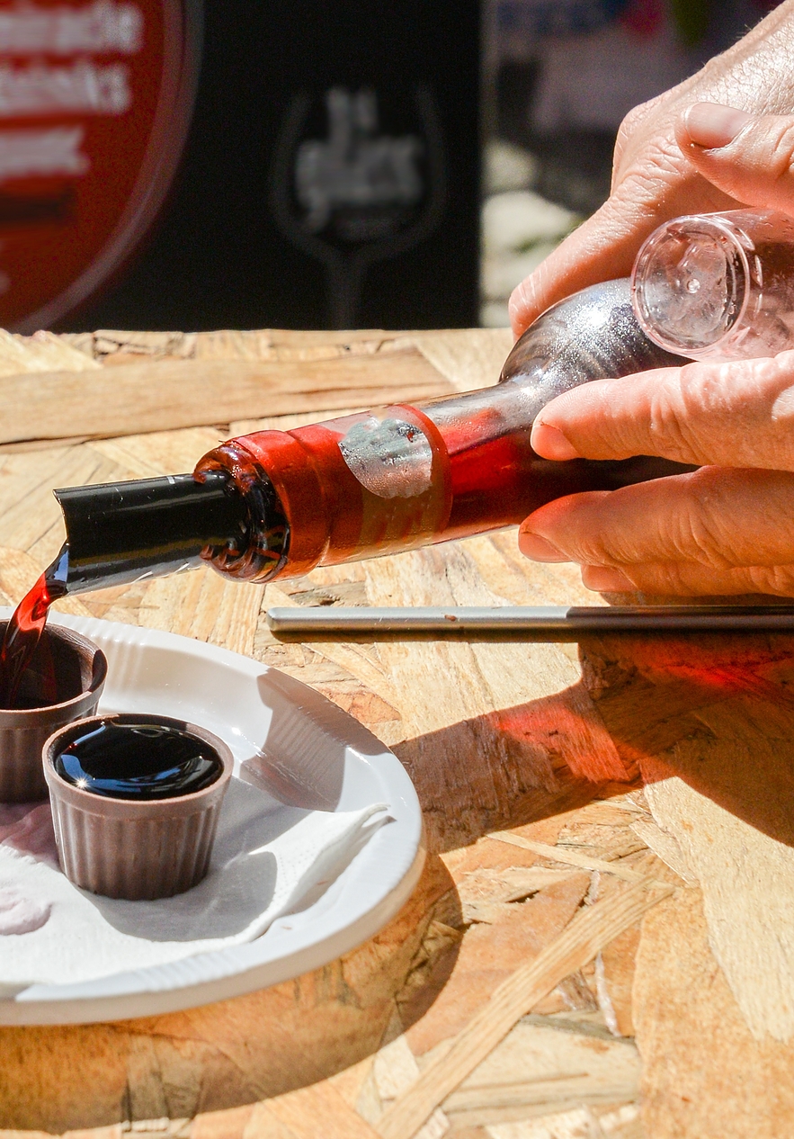 A hand holds a bottle of ginjinha while pouring the liquid into two small glasses