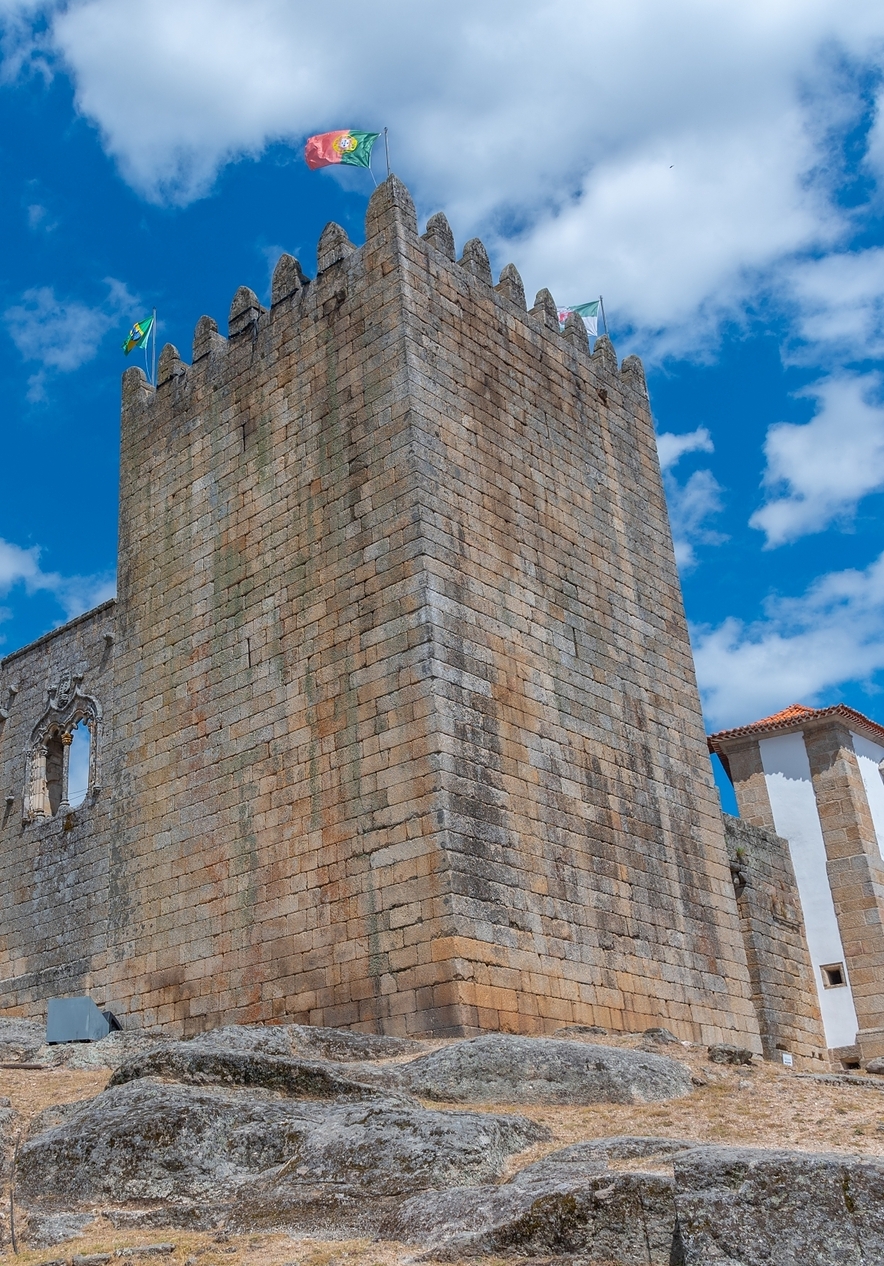 View of the outside of Belmonte Castle with a tall tower and a flag of Portugal on top