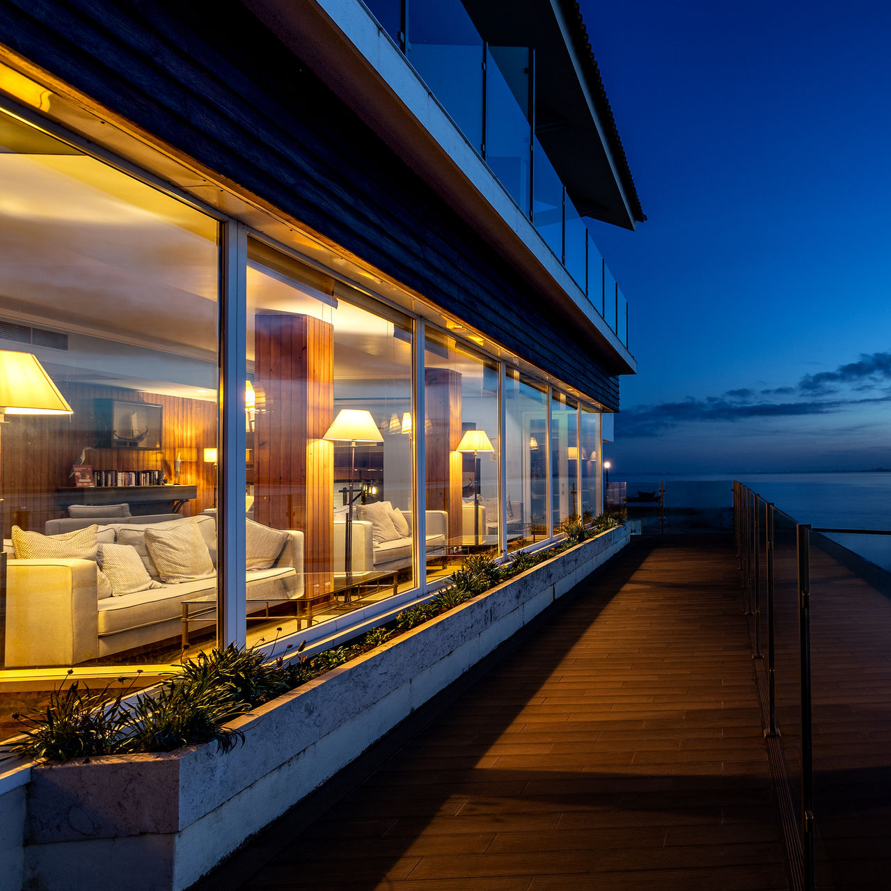 Outdoor patio of Pousada Ria - Aveiro, with large windows overlooking the lagoon at sunset and a wooden deck