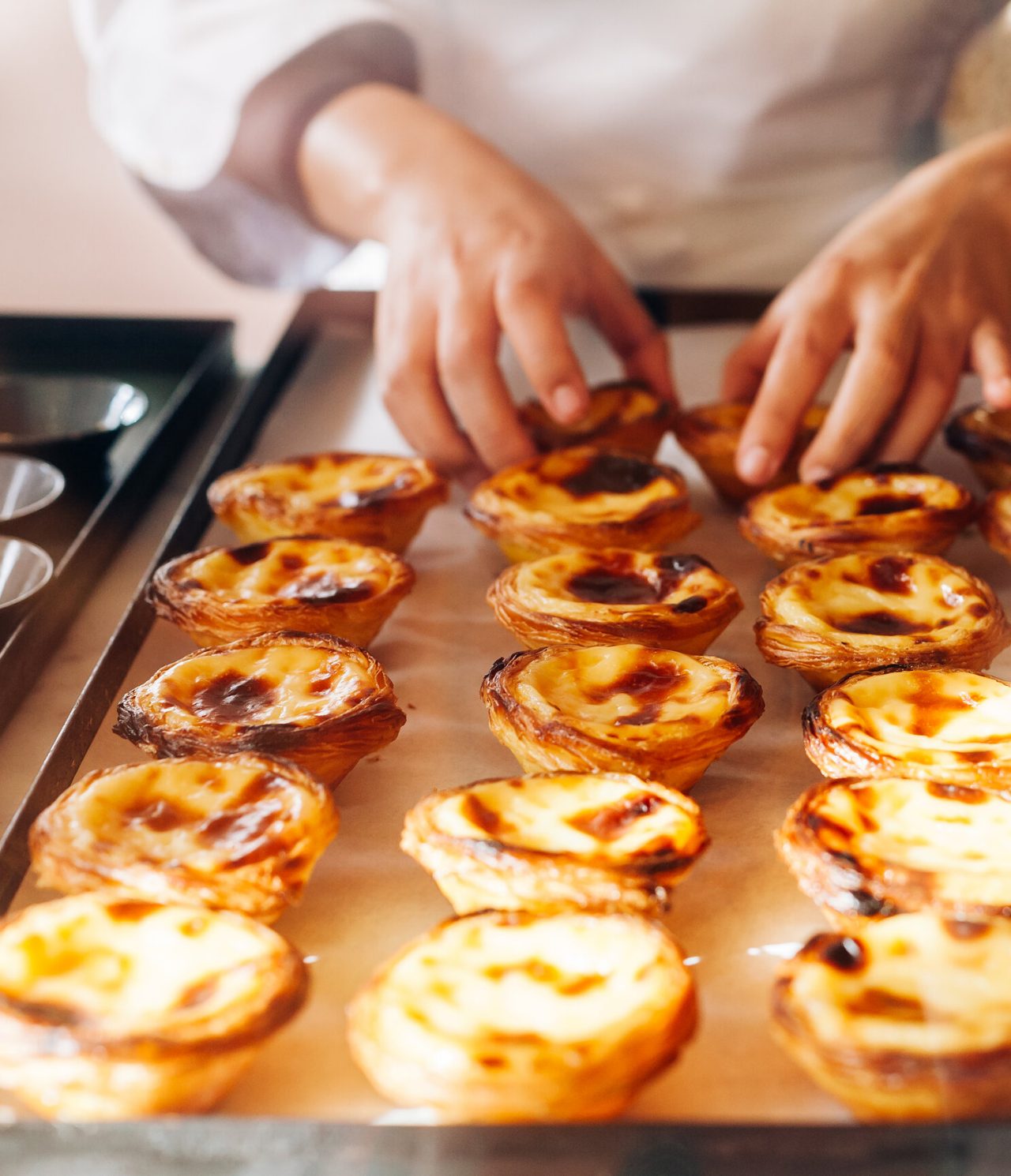 Explore Hotels in Lisbon featuring freshly baked custard tarts arranged on trays beside a pastry chef