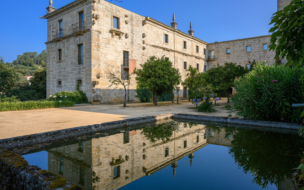 Vista exterior do edifício da Pousada Mosteiro Amares, um Hotel Histórico no Gerês, em pedra com um lago em frente