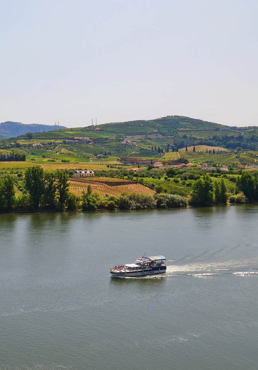 Lonely boat sailing on the Douro river with vegetation and some houses in the background in Peneda-Gerês