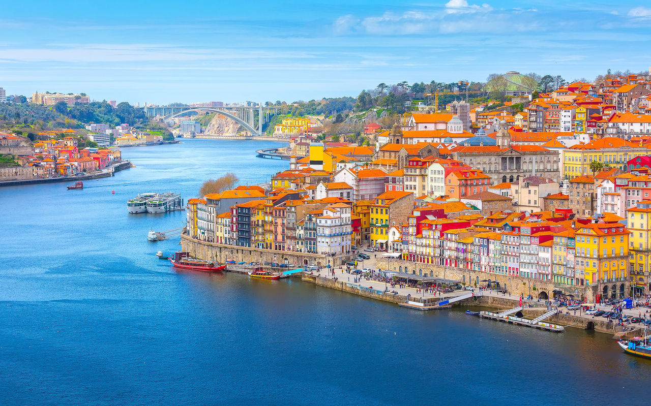 Explore Hotels in Porto featuring colorful riverside buildings, boats and the Dom Luís bridge skyline