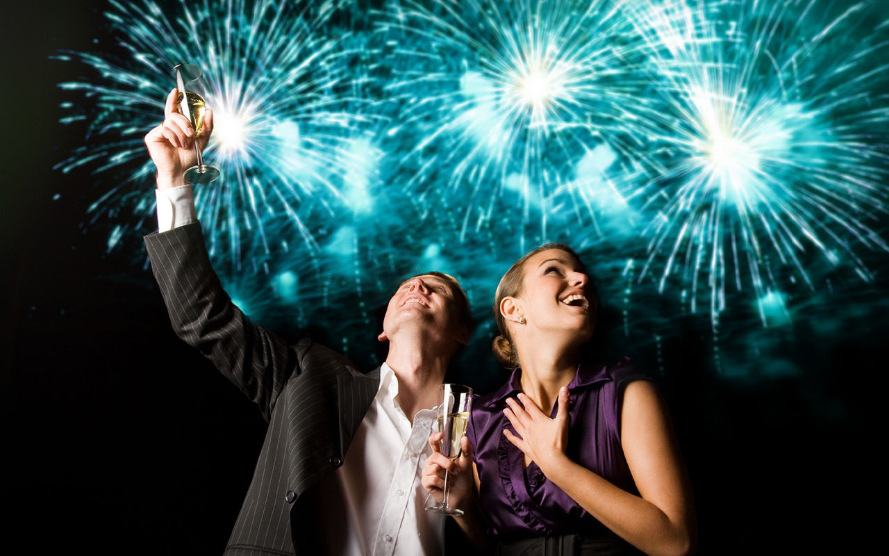 Couple celebrating the New Year, with blue fireworks behind, at a party in a Pestana Hotel Group hotel