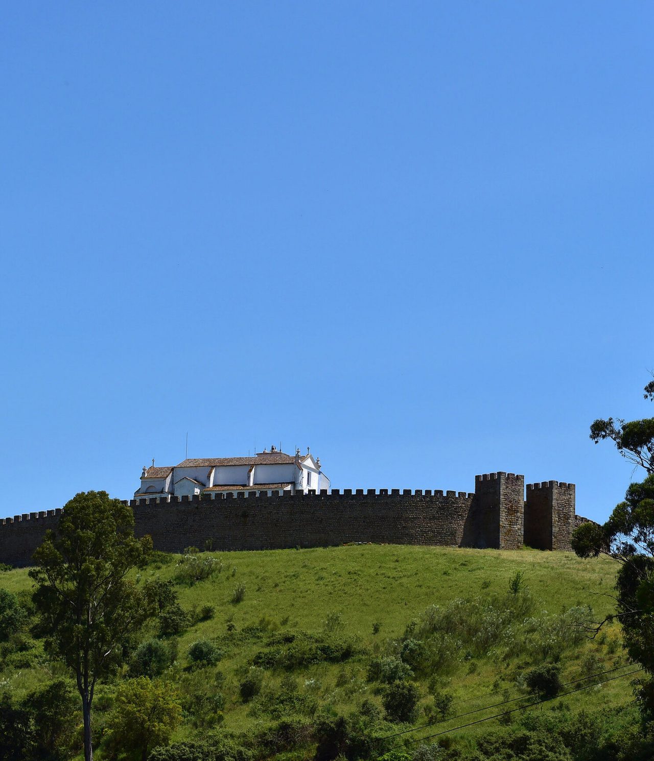 Castillo histórico en la cima de una colina en Arraiolos, Alentejo, rodeado de paisajes verdes y un cielo azul claro