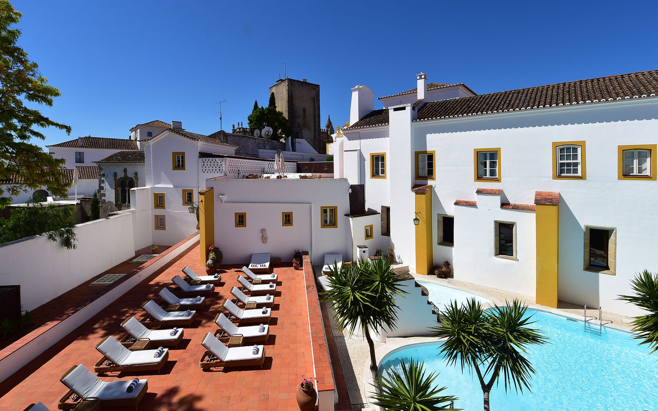 Vista de la piscina, las tumbonas y el edificio de Pousada Convento de Évora, un hotel con piscina en Évora, Alentejo
