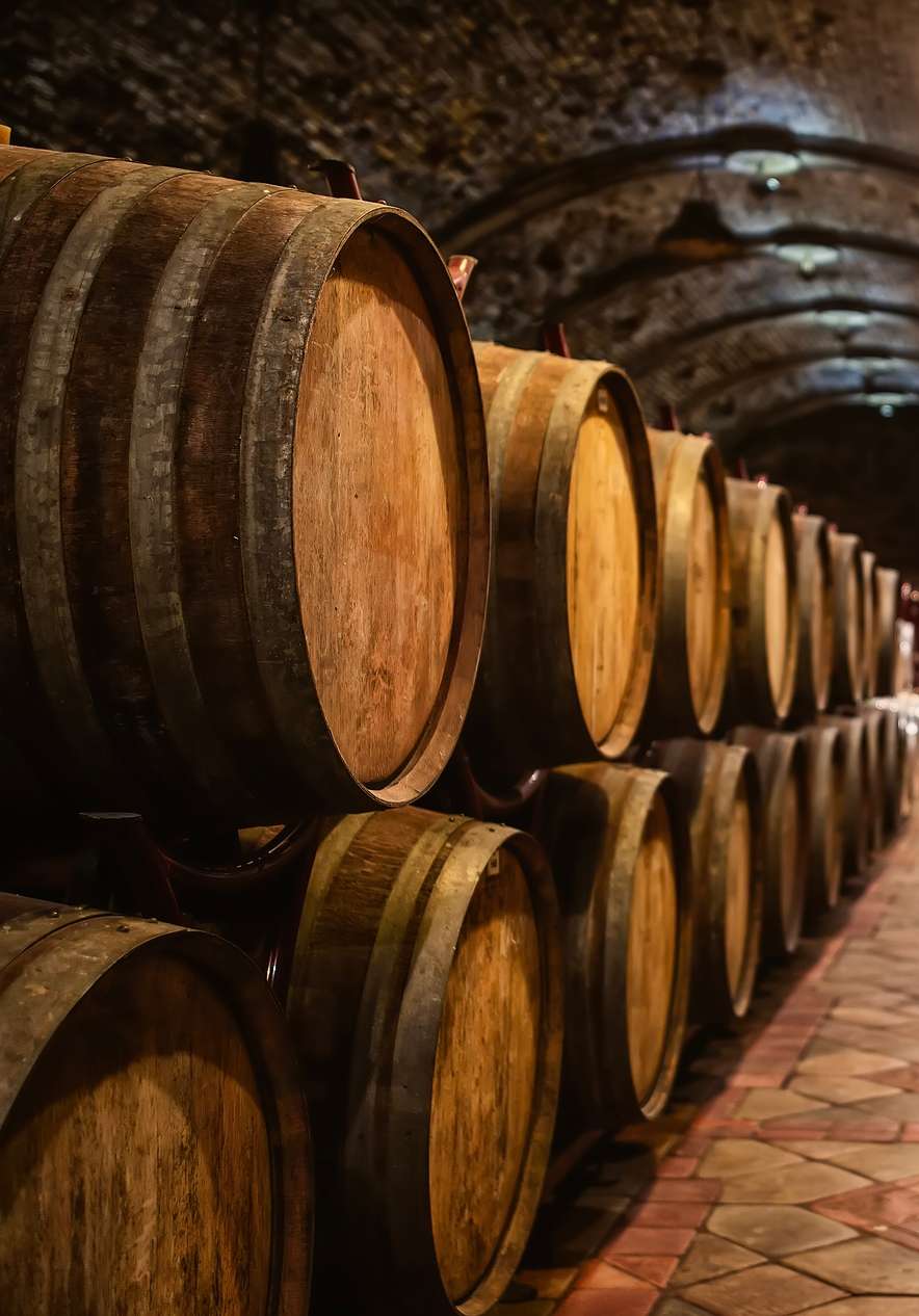 Interior de una bodega de vino tradicional, con barricas apiladas y paredes de ladrillo con luces colgantes
