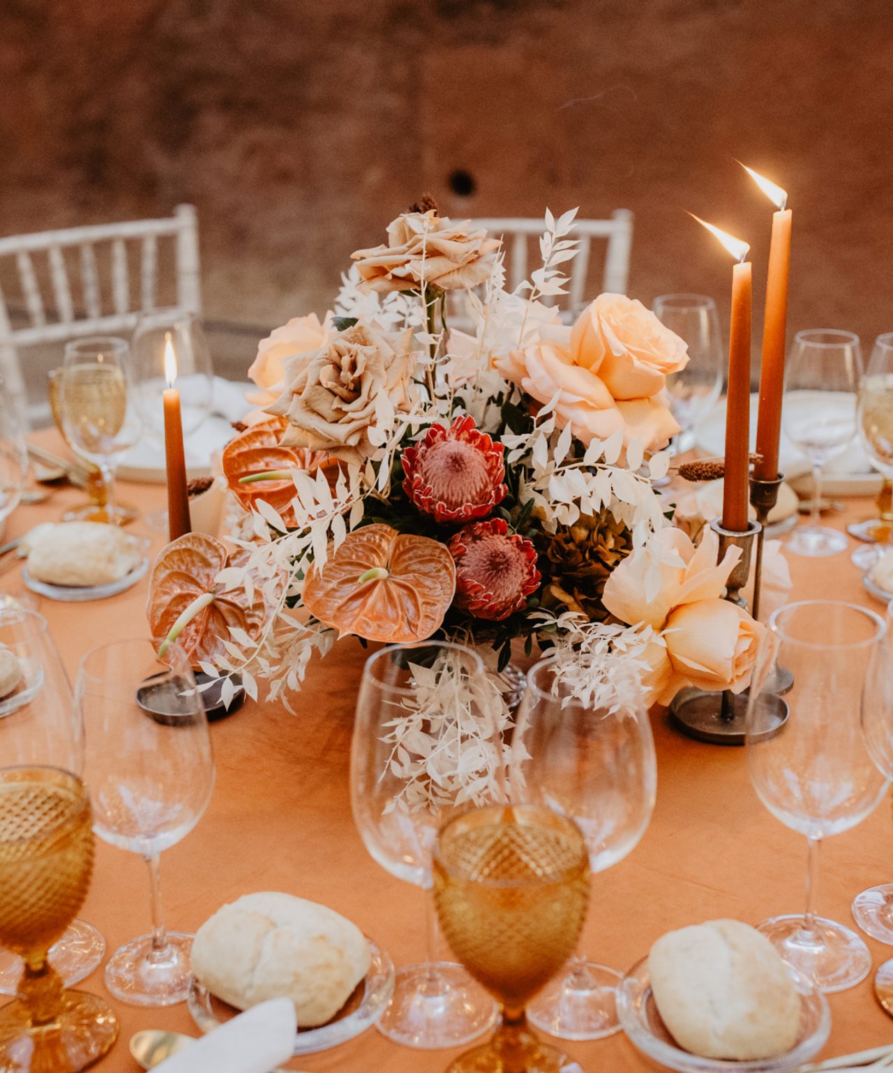 Mesa de boda con decoración elegante, con centro de mesa con flores y velas de color naranja oscuro