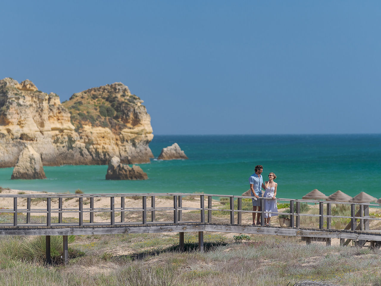 Couple admirant la vue d'une plage à Alvor, Algarve, tout en se promenant sur les passerelles au bord de la mer