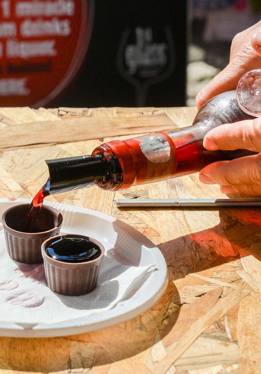 Une main tenant une bouteille de ginjinha, versant le liquide dans deux petits verres