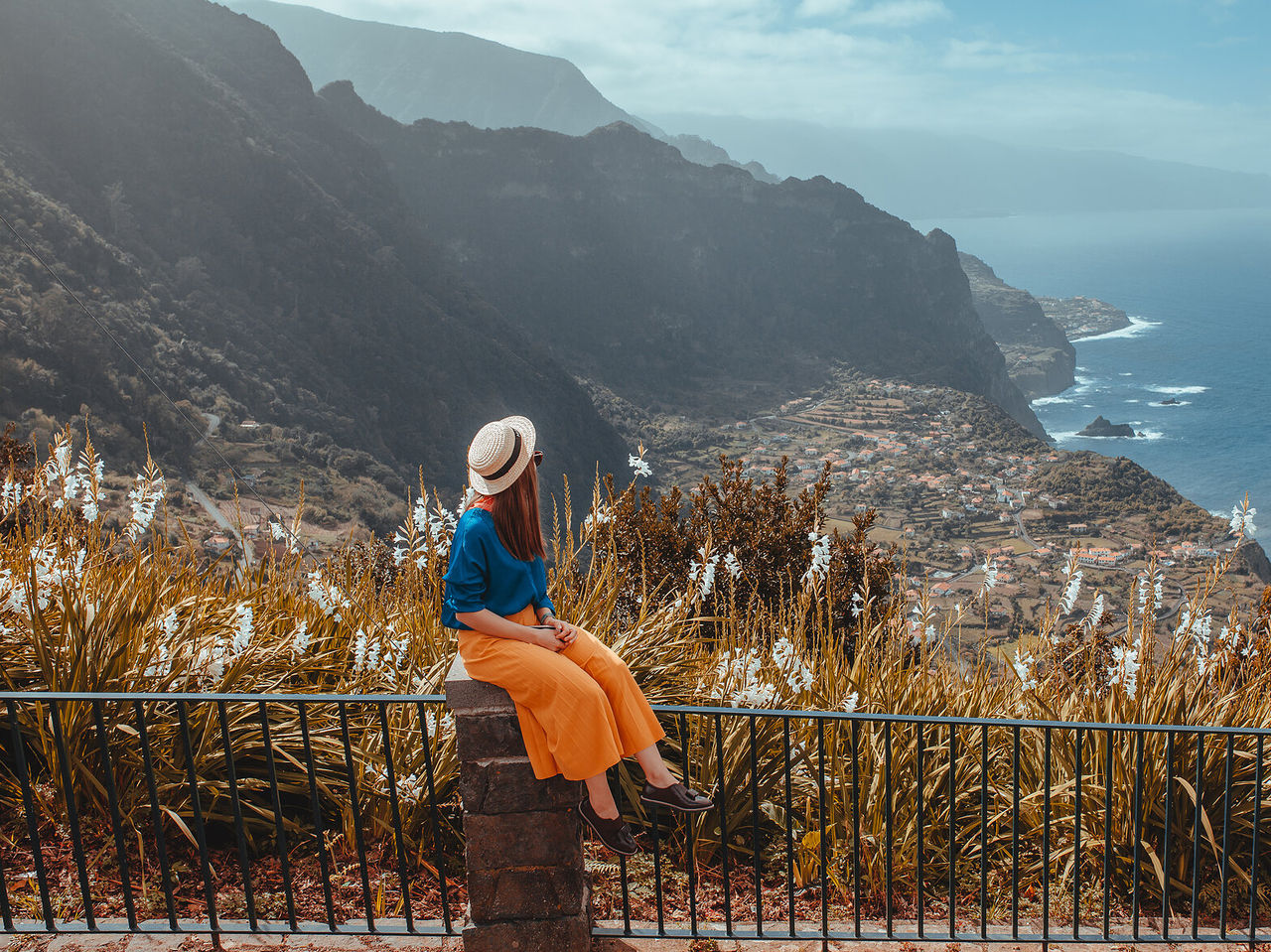 Femme assise sur un mur apprécie la vue d'une fajã sur l'île de Madère, avec la mer l'entourant