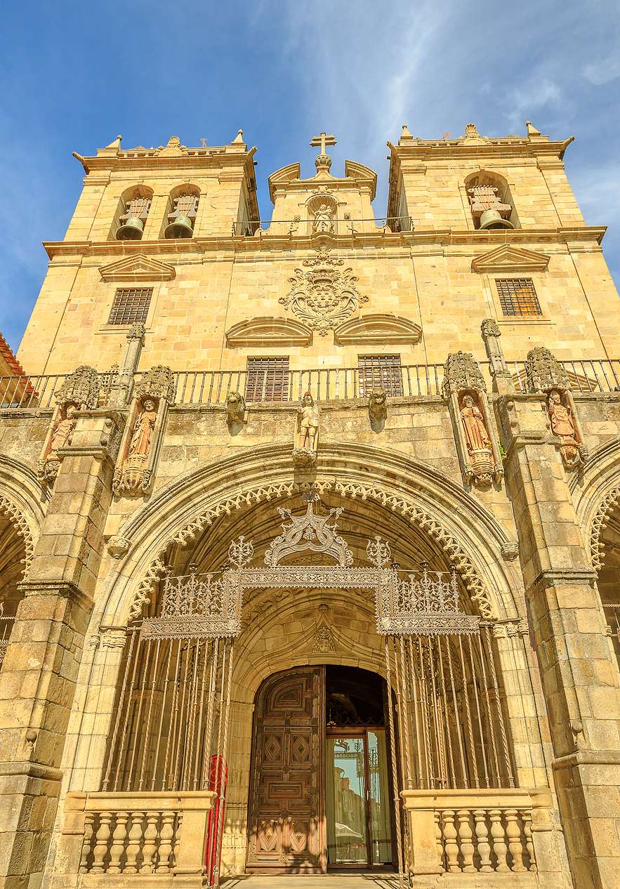 Vue frontale de la façade de la Cathédrale de Braga, avec une grande porte et de nombreux détails travaillés