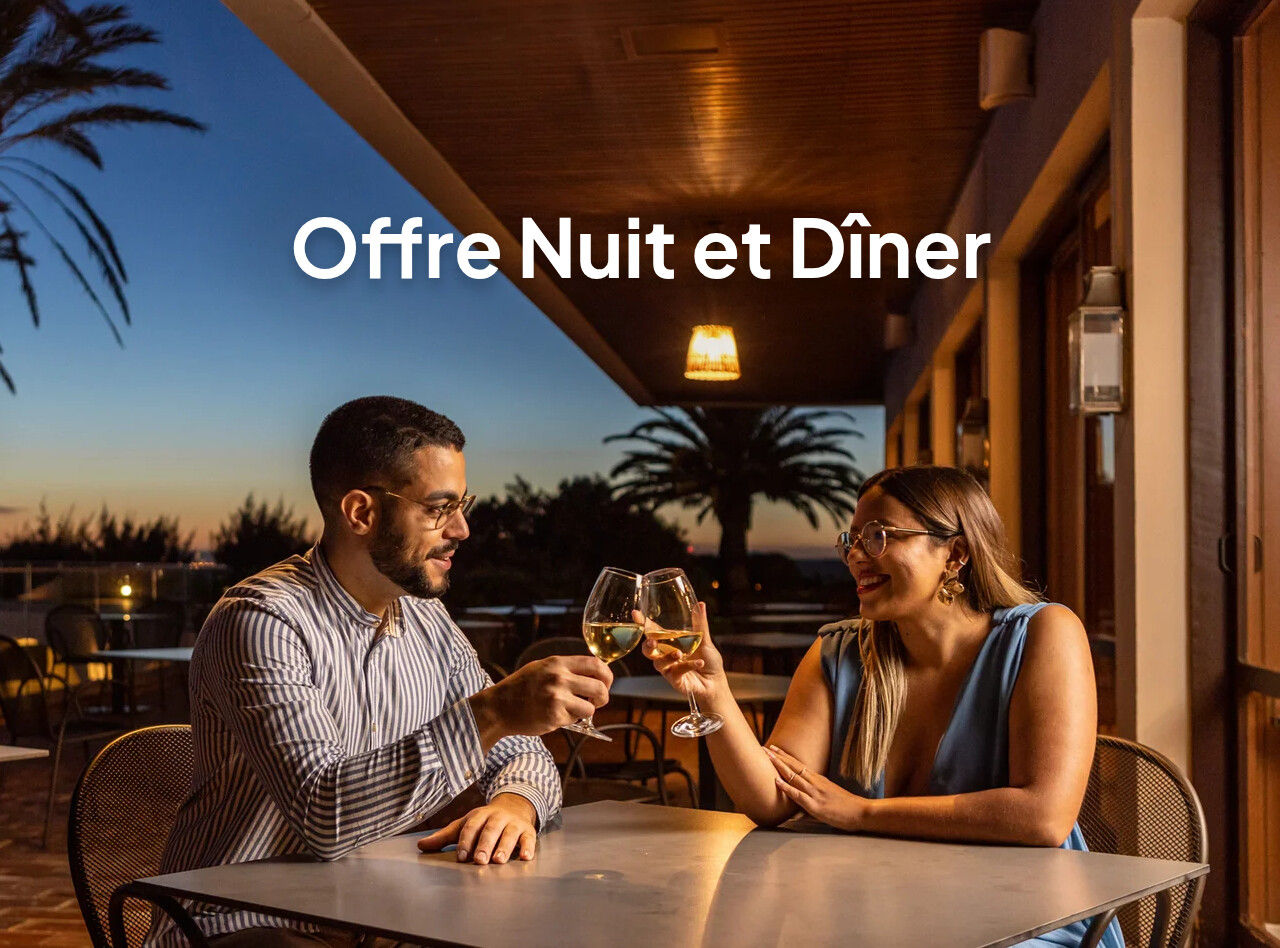 Couple levant des verres de vin sur une terrasse éclairée au coucher du soleil avec des palmiers en arrière-plan