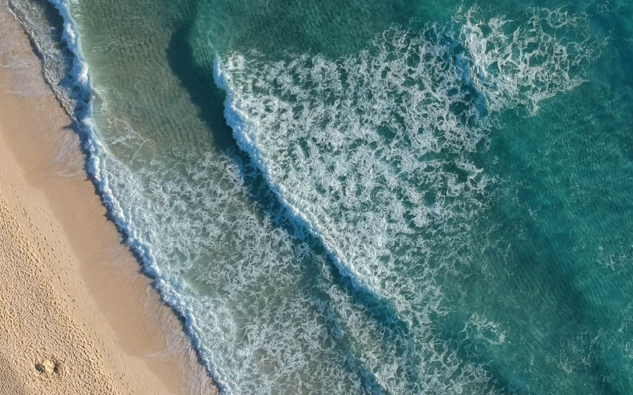Luchtfoto van een strand met golven die breken op het gouden zand, in een hotel van de Pestana Hotel Group