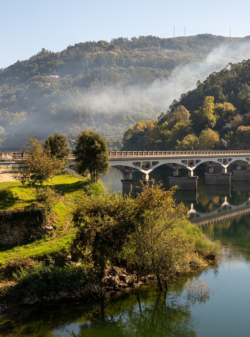 Paisagem do norte de Portugal com uma ponte de pedra sobre um rio, cercada por colinas verde
