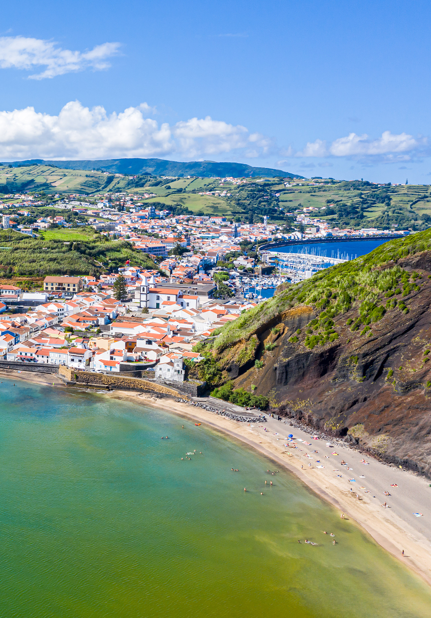 Vista aérea da baía da cidade da Horta, na ilha do Faial, nos Açores, com casas coloridas, e uma praia de areia escura