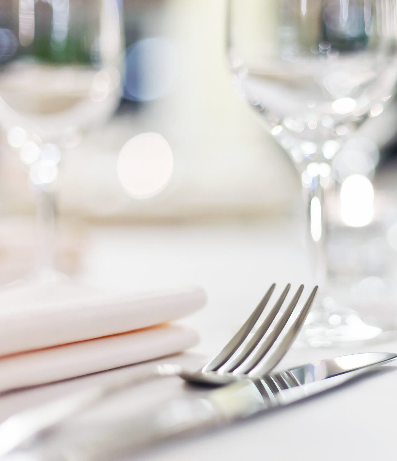 Explore Hotéis no Alentejo apresentando mesa elegante com talheres, guardanapos e copos desfocados sobre mesa branca