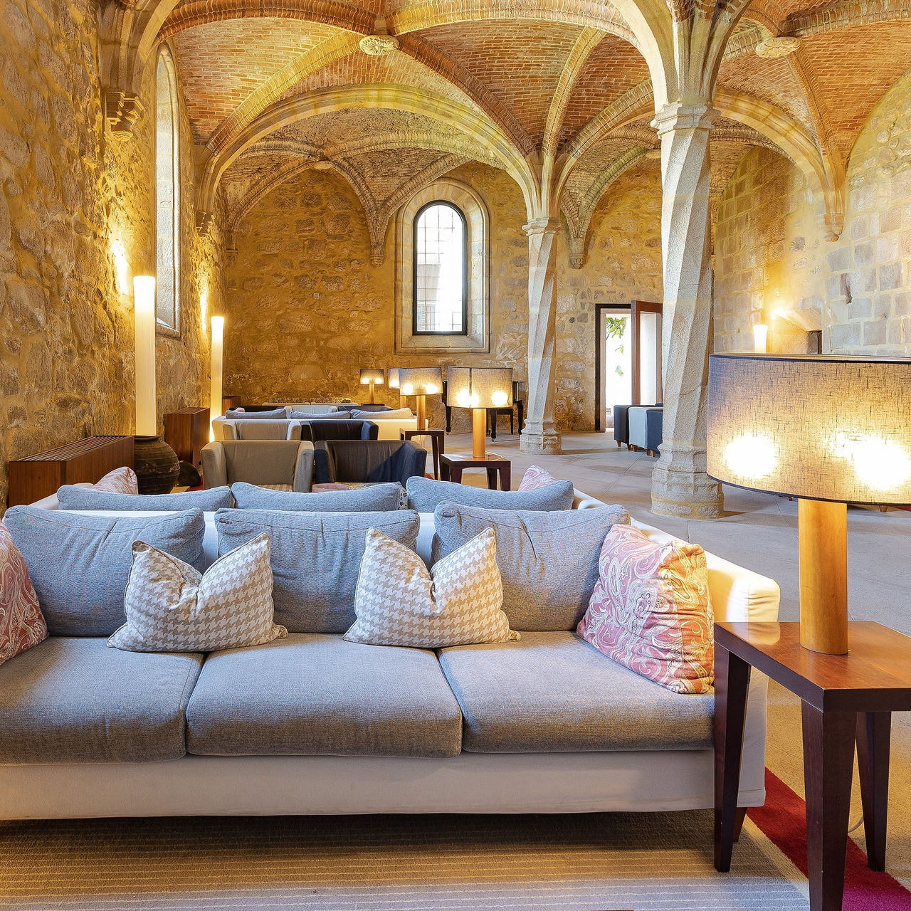 Interior imponente do histórico Pousada Mosteiro do Crato, com tetos altos abobadados, paredes de pedra e sofás para relaxar
