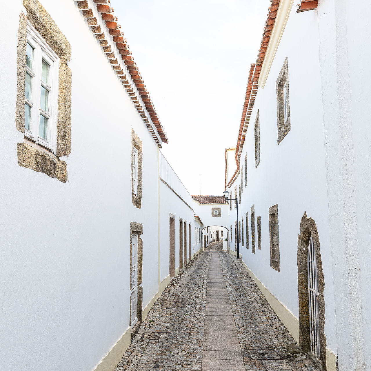 Vista de uma rua estreita, perto da Pousada Marvão, um Hotel Histórico em Marvão, com paredes brancas e detalhes em pedra