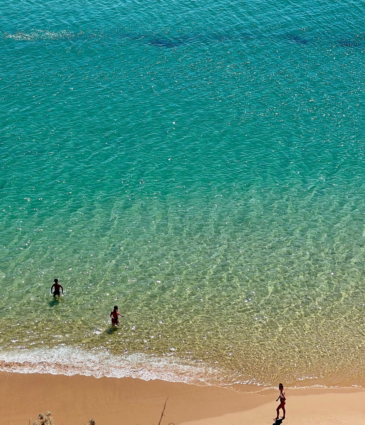 Vista aérea de duas pessoas a nadar numa praia em águas cristalinas e com areia dourada, na região do Algarve