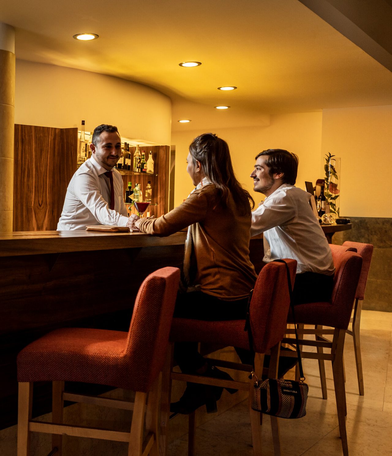 O bar Pousada Convento Tavira, do Hotel no Centro Histórico de Tavira, tem um casal sentado, a ser servido de cocktails