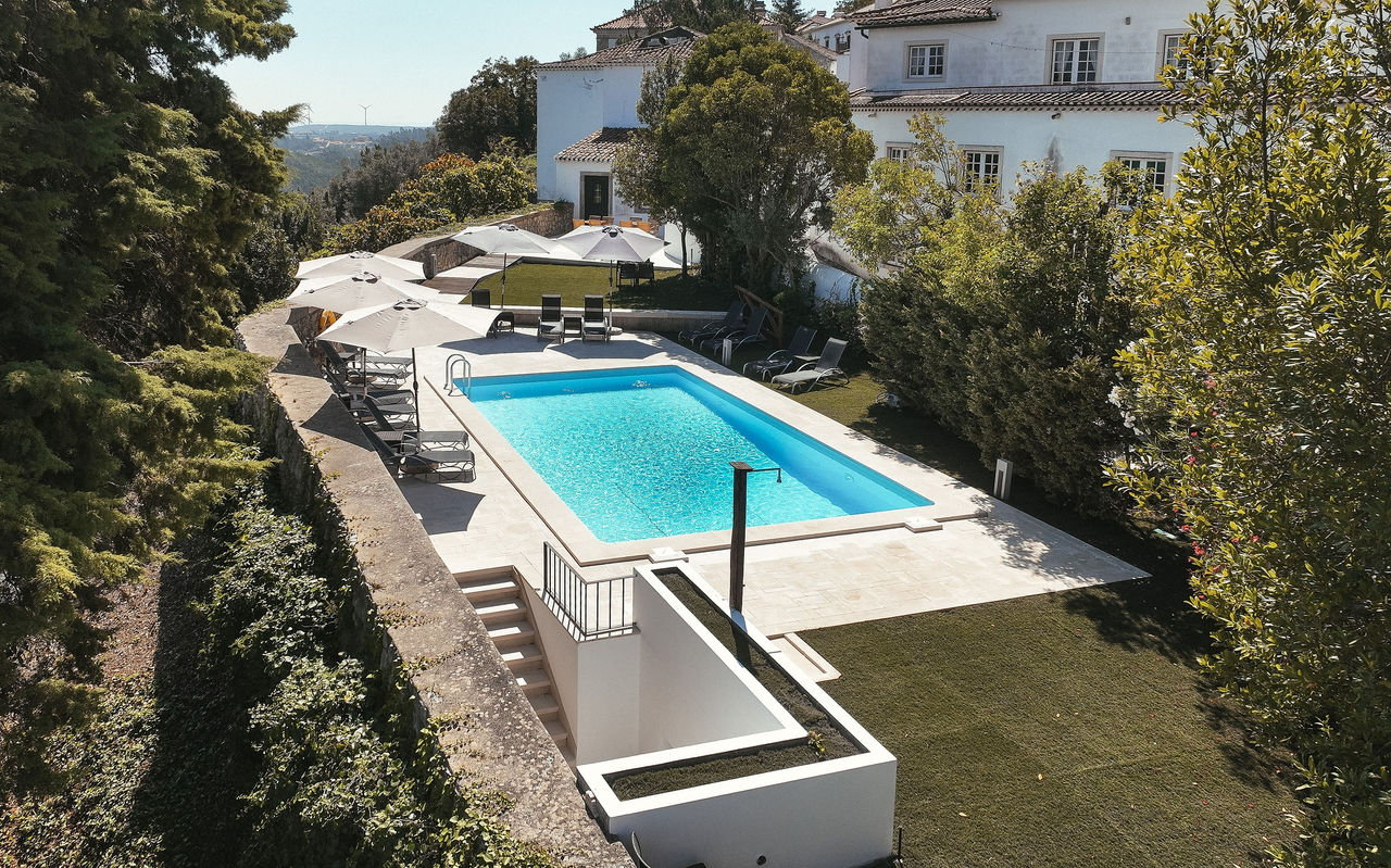 Vista para a piscina exterior da Pousada Ourém, um hotel de charme perto de Fátima, com espreguiçadeiras e chapéus de sol