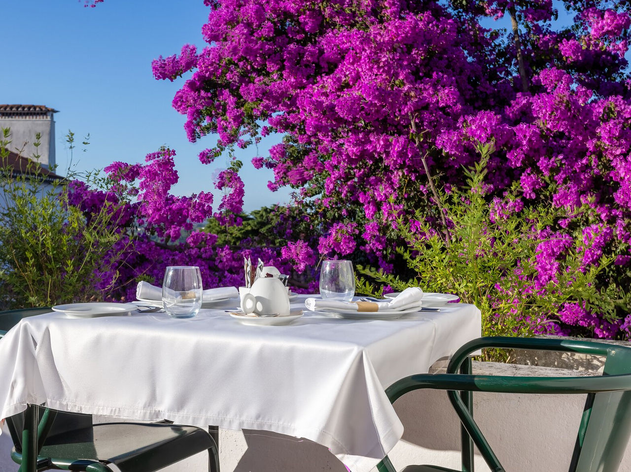 O restaurante do Hotel de Charme em Ourém, tem uma mesa preparada para o pequeno-almoço com árvore com flores violeta atrás