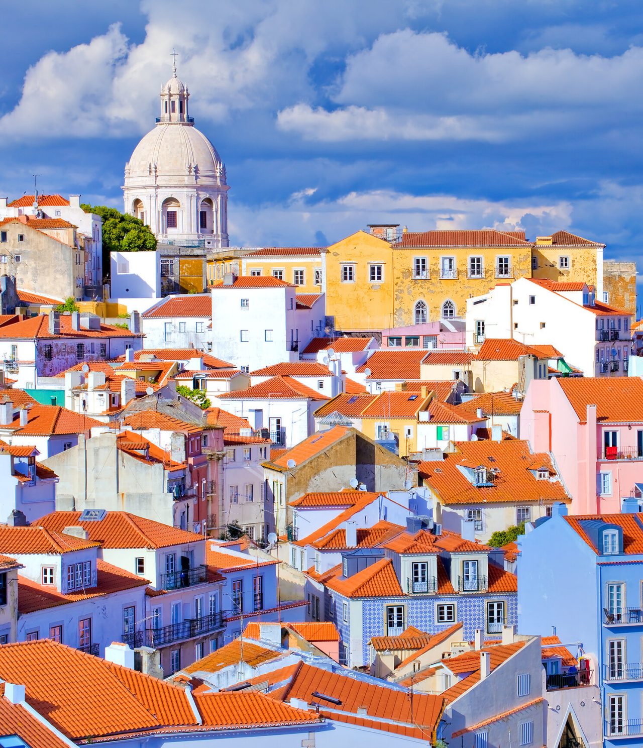 Centro histórico de Lisboa, com vários prédios típicos, com telhados em tijolo e uma basílica ao fundo