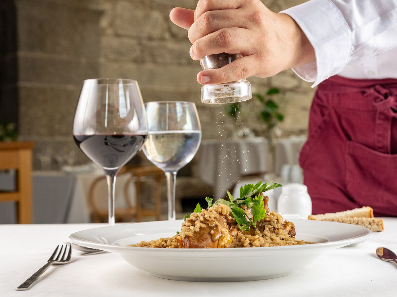 Prato de arroz com carne, sendo temperado com pimenta moída por um empregado de mesa, a acompanhar com um copo de vinho