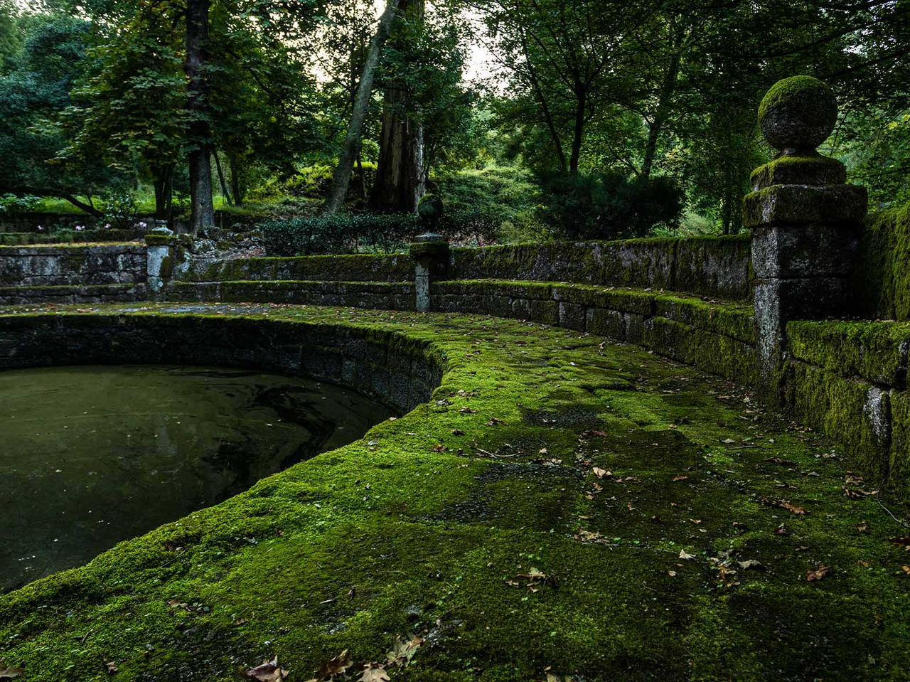 Jardim histórico da Pousada Mosteiro de Guimarães com muros de pedra cobertos de musgo e árvores ao fundo