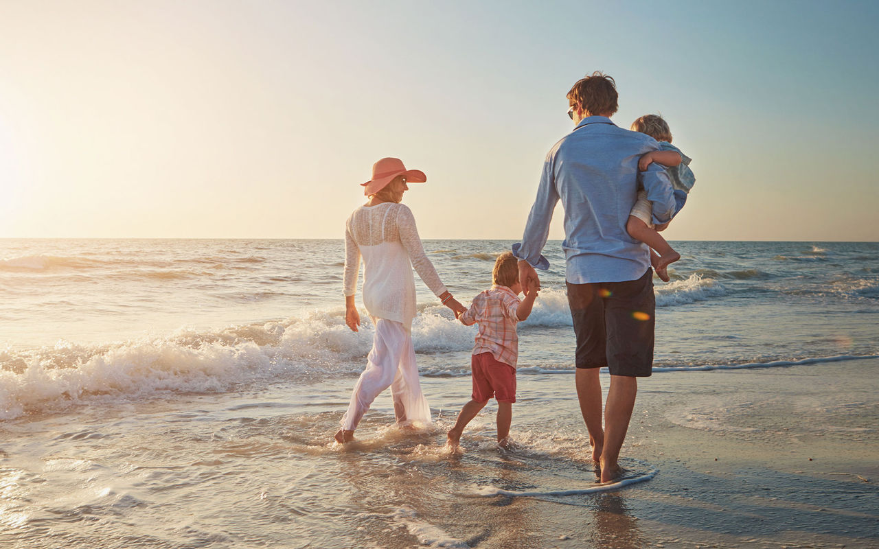 Descubra Pousadas de Portugal onde uma família caminha junto ao mar ao pôr do sol numa praia tranquila