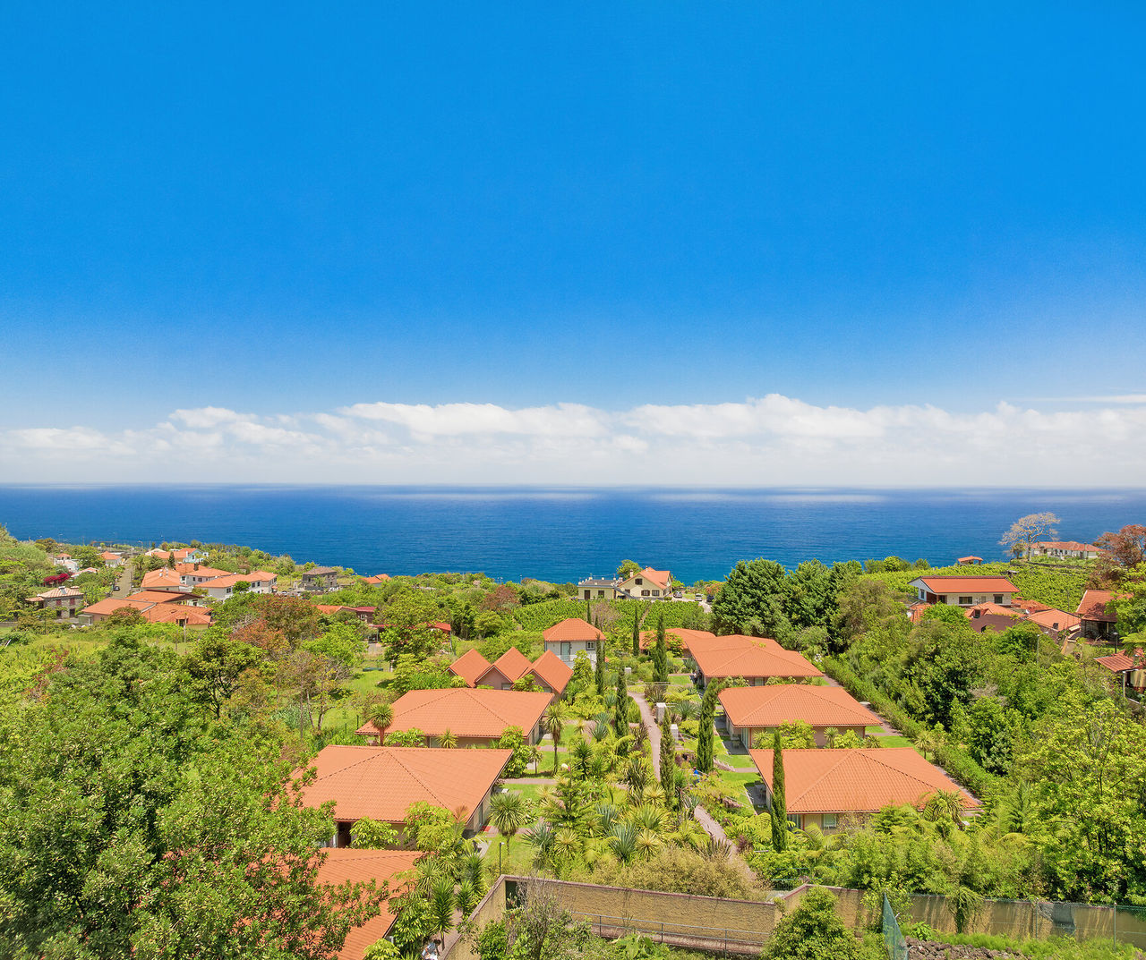 madeira hotel com vista para villas de telhados vermelhos entre jardins verdes junto ao oceano azul e céu limpo