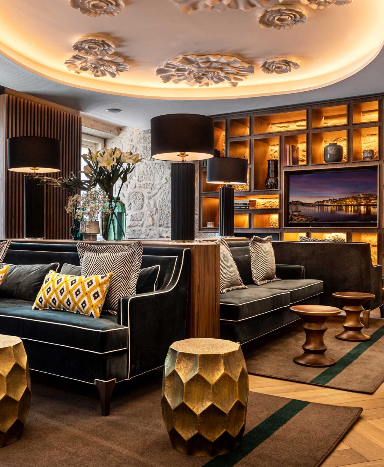 Sala de estar elegante com sofás escuros, almofadas geométricas, candeeiros pretos e decoração dourada