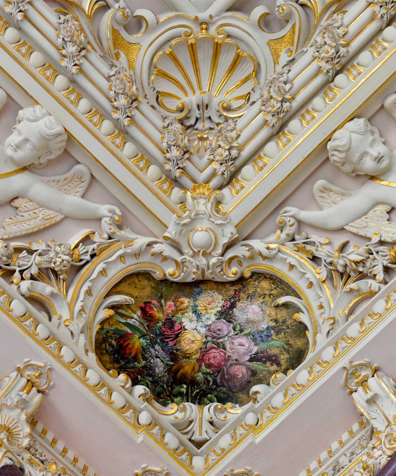 Detalhe de teto ornamentado com molduras douradas e pintura floral cercada por esculturas de anjos