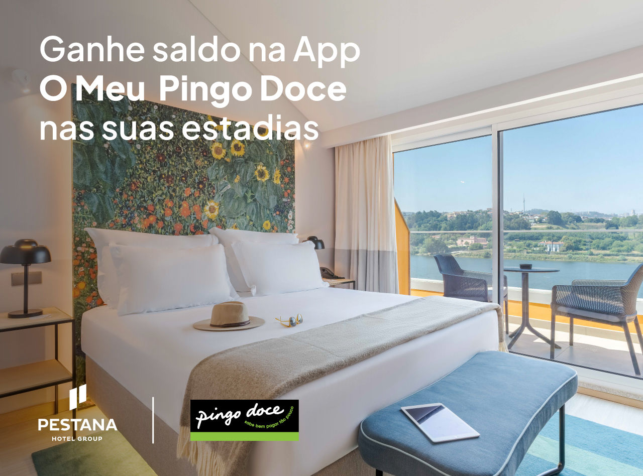 Quarto de hotel com cama ampla, parede floral e varanda com vista para o rio e cadeiras ao ar livre