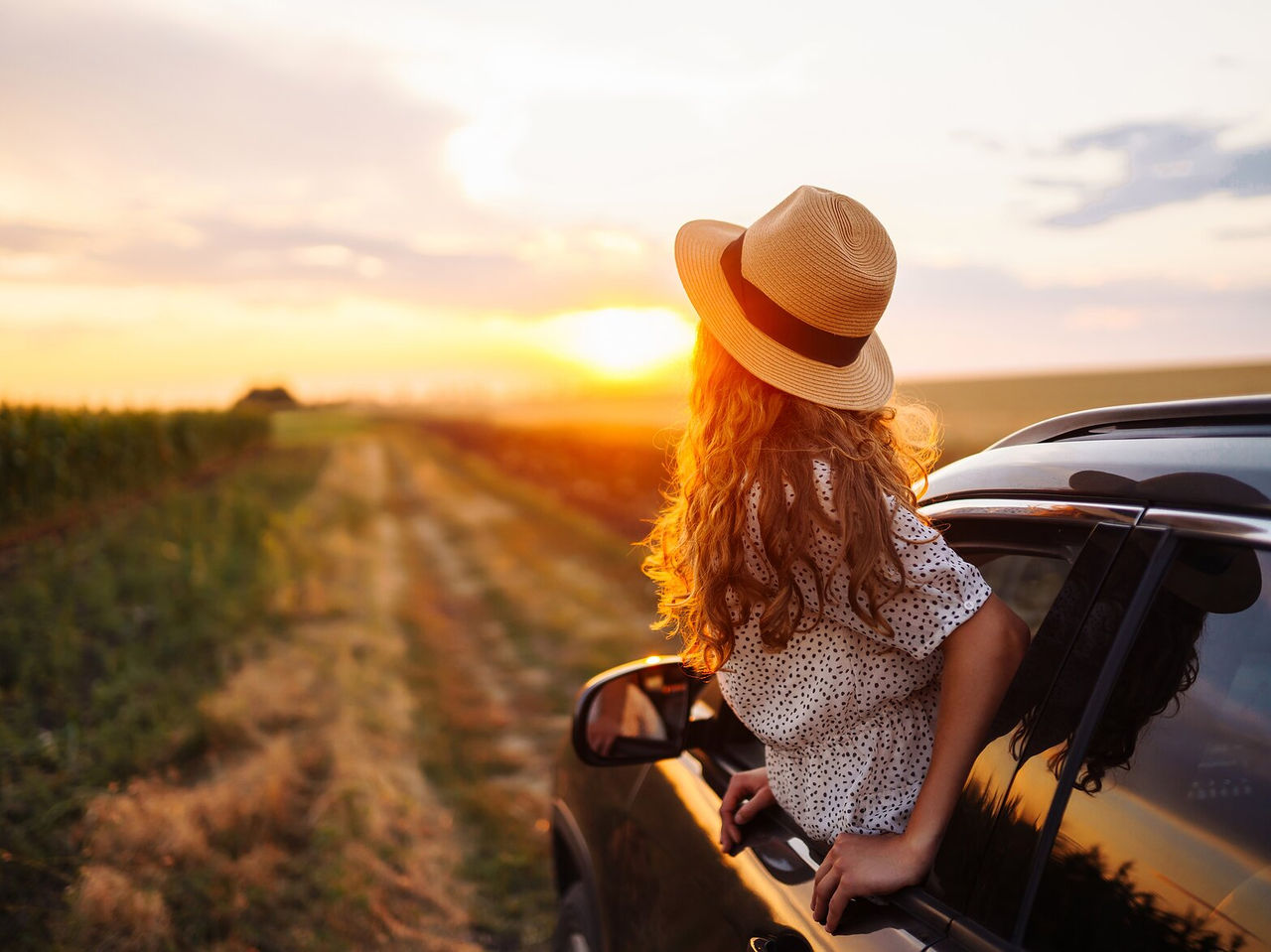 Explore Hotels in Alentejo featuring a traveller watching the sunset beside a car on a rural vineyard road